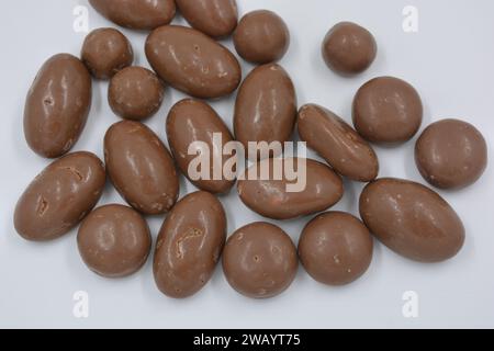 Cioccolatini, arachidi, noci, uva passa ricoperta di glassa al cioccolato, ciottoli di cioccolato disposti su sfondo bianco. Foto Stock