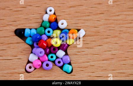 Perline colorate utilizzate per creare collane e braccialetti che formano una stella su sfondo di legno Foto Stock