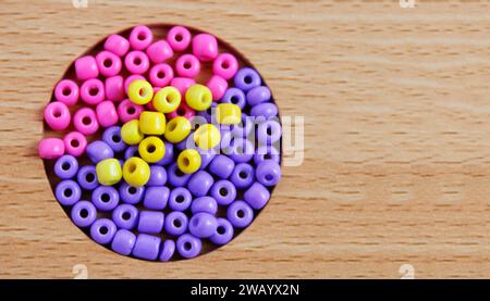 Perline colorate utilizzate per creare collane e braccialetti che formano un cerchio su sfondo di legno Foto Stock
