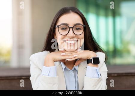 Una giovane donna allegra con gli occhiali che posano il mento sulle mani, indossando uno smartwatch Foto Stock