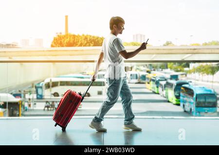 Vista laterale di un turista asiatico che cammina all'aeroporto con smartphone Foto Stock