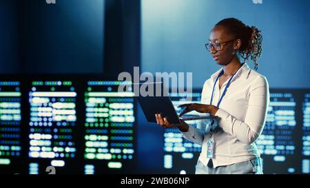 Programmazione di computer scientist in server farm che ospita apparecchiature avanzate che memorizzano enormi set di dati. Sviluppatore che esegue codice su notebook per riparare i rack dei data center eseguendo complesse operazioni di calcolo Foto Stock