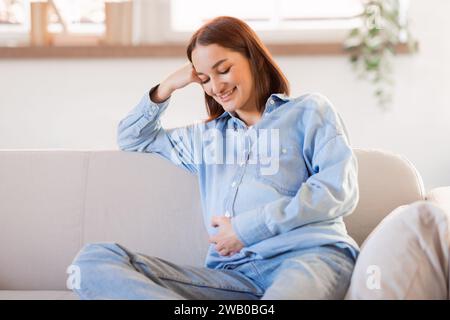 Donna incinta sorridente in un ambiente informale che riposa sul divano a casa Foto Stock
