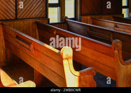 L'interno di una chiesa d'epoca con panche in legno o panche in legno rosso. Le travi di sole brillano nel vecchio edificio attraverso un alto vento di vetro trasparente Foto Stock