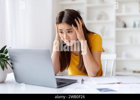 Stress della scadenza. Una donna asiatica scioccata che guarda lo schermo del notebook e tocca la testa Foto Stock