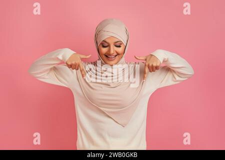 Femmina musulmana positiva in Hijab che punta verso il basso con due mani Foto Stock