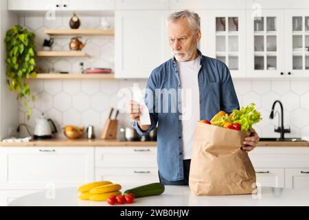 Signore anziano in cucina, con borsa di generi alimentari e ricevuta della spesa Foto Stock