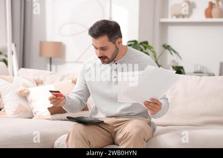 Uomo confuso con notifiche di debito, calcolatore e budget di pianificazione della carta di credito a casa. Problema finanziario Foto Stock
