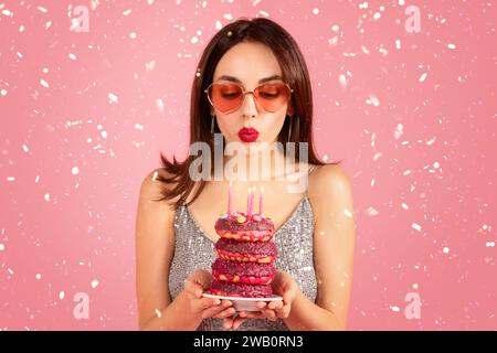 Felice donna millenaria caucasica in vestito, gli occhiali sprigionano le candele fa un desiderio Foto Stock