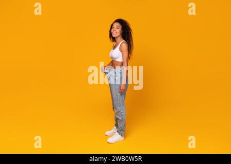 Donna nera felice che mostra la perdita di peso indossando pantaloni oversize, studio Foto Stock