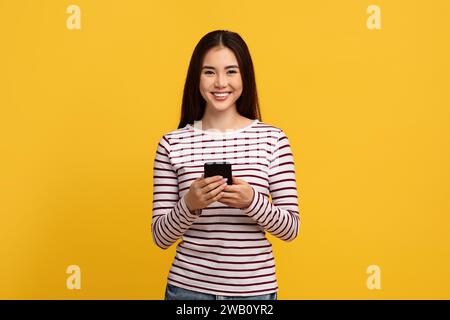 Carina giovane donna asiatica che tiene il cellulare Foto Stock