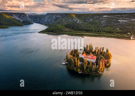 Visovac, Croazia - veduta aerea dell'isola del monastero cristiano di Visovac nel Parco Nazionale di Krka in una soleggiata mattinata autunnale con drammatica alba dorata e. Foto Stock