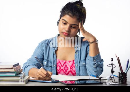 Un giovane studente indiano che studia e scrive su un tavolo da studio e su uno sfondo bianco Foto Stock