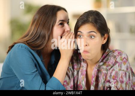 Gossip donna che dice segreto a un amico perplesso a casa Foto Stock