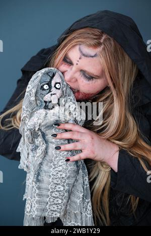 Una cosplayer femminile in un costume da strega fantasy con una strana bambola Foto Stock