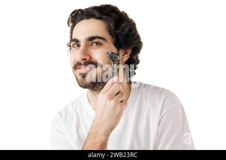 Ritratto dell'uomo si muove senza problemi sulla pelle del viso con il rullo massaggiante su sfondo bianco. Concetto di routine per la cura del viso. Foto Stock