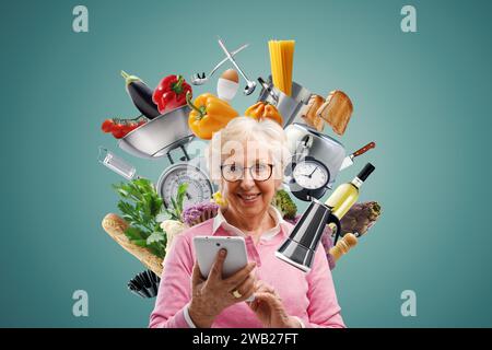 Donna anziana felice circondata da cibo e utensili da cucina, sorride e utilizza un tablet digitale: Concetto di cucina e ricette online Foto Stock