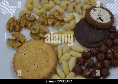 Cibo sano e salutare, snack, tante noci naturali: Anacardi, mandorle, noci, nocciole e biscotti posti su un piatto di vetro bianco. Foto Stock