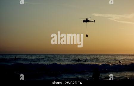 Rio de Janeiro, Rio de Janeiro, Brasile. 7 gennaio 2024. Il Rio de Janeiro Air Sea Rescue ha eseguito con successo un'operazione di salvataggio al tramonto sulla spiaggia di Ipanema, salvando un nuotatore in difficoltà. Sullo sfondo delle pietre di Arpoador, un elicottero ha portato l'individuo salvato davanti a centinaia di persone che si riuniscono ogni giorno per assistere agli splendidi tramonti. Questo incidente ha sottolineato l'intensa attività nelle acque di Rio dall'inizio del nuovo anno, con un notevole aumento delle operazioni di salvataggio che rispondono alle condizioni di surf. (Immagine di credito: © Bob Karp/ZUMA Press Wire) SOLO USO EDITORIALE! Foto Stock