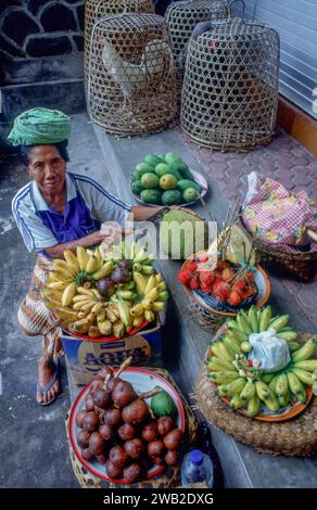 Indonesia, Tirtaganga. Donna che vende jackfruit, salak bali, frutta serpente, banane, mango e rambutan Foto Stock
