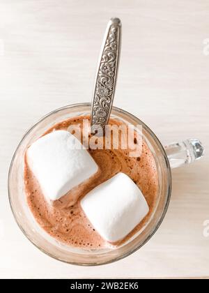 Cioccolata calda con due marshmallow e cucchiaio in tazza di vetro Foto Stock