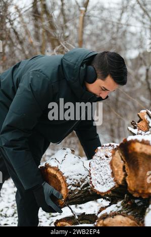 Giovane uomo che raccoglie tronchi di legno in condizioni di neve per utilizzarli successivamente come legna da ardere Foto Stock