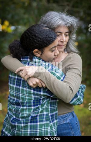 Una madre bianca abbraccia e conforta la sua figlia adolescente birazziale Foto Stock