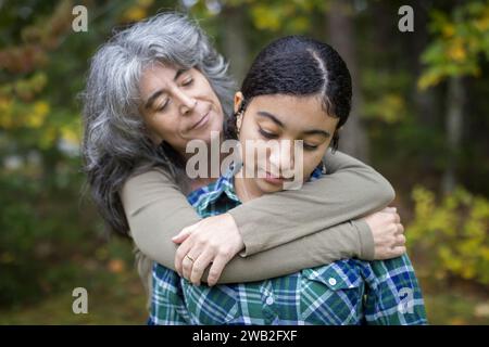 Una madre bianca abbraccia e conforta la sua figlia adolescente birazziale Foto Stock