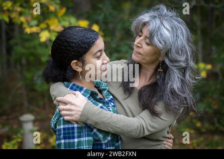 Una madre bianca mette le braccia intorno alla sua figlia adolescente birazziale Foto Stock