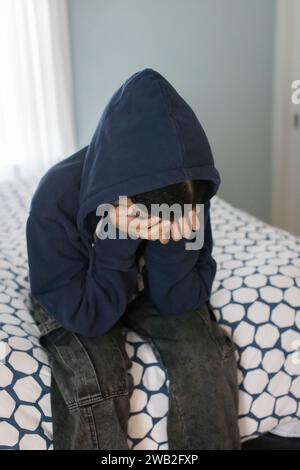 Adolescente birazziale siede sul letto con la testa nelle mani che sembra depressa Foto Stock