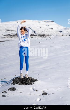 Una verticale di una giovane donna si erge su una roccia innevata in un paesaggio montano Foto Stock