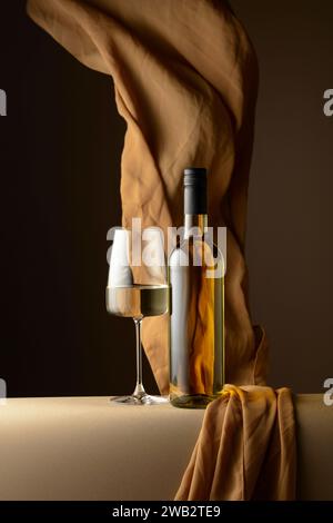 Bottiglia e bicchiere di vino bianco e flutti di panno beige su sfondo scuro. Copia spazio. Foto Stock