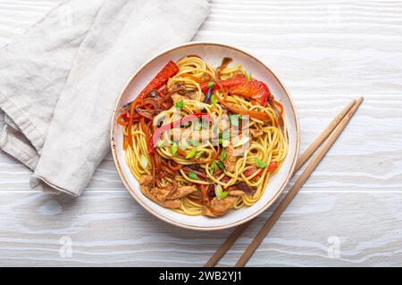 Ciotola bianca con Chow Mein o lo Mein, spaghetti tradizionali cinesi con carne e verdure, serviti con bacchette e vista dall'alto su rustico bianco Foto Stock