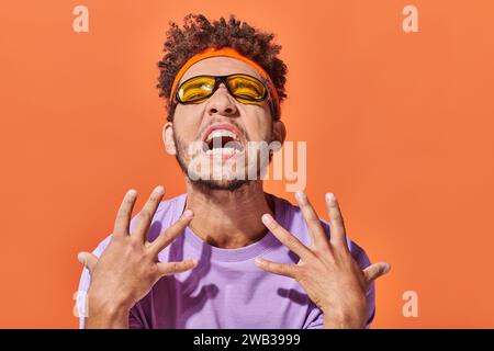 emotivo uomo afroamericano con fascia e occhiali da sole che gestiscono su sfondo arancione Foto Stock