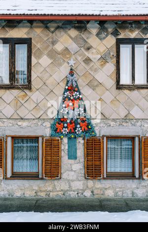 L'albero di Natale Felt con archi rossi e ghirlande appese alla facciata della casa Foto Stock