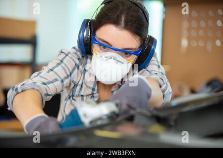 lavoratrice donna che utilizza una smerigliatrice angolare e indossa una maschera Foto Stock