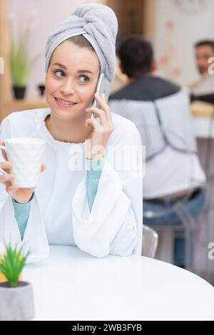 avvolta in un asciugamano donna che beve tè al telefono Foto Stock