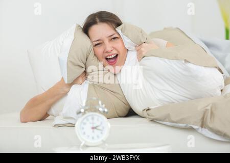 una giovane donna che tiene i cuscini sulle orecchie per affogare l'allarme Foto Stock