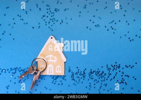 Chiave con casa dei giocattoli in legno su sfondo blu con stelle scintillanti, posizione piatta Foto Stock