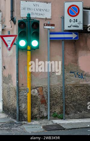 Due semafori verdi e diversi segnali stradali in una stradina. Foto Stock