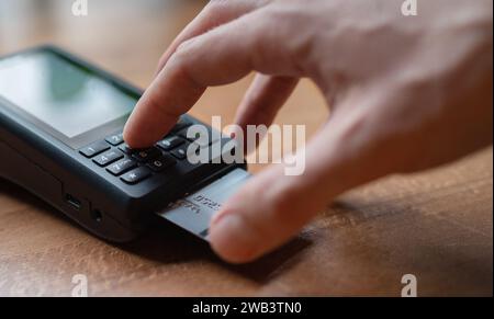 Man palm Typing POS terminal buttons credito pin-code effettuando pagamenti bancari wireless con processo Acquisisci al ristorante Table Cafe al coperto. Concentrati sul machin Foto Stock