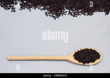Riso nero in cucchiaio di legno. Riso nero sparso su sfondo grigio. Copia spazio. Spianatura piatta Foto Stock