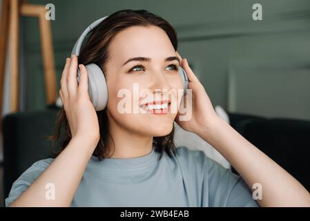 Una giovane donna sorridente di mezza età che indossa cuffie wireless ascolta la musica. Beatitudine musicale. Donna di mezza età che abbraccia Joy tramite wireless Foto Stock