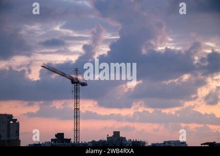 Una torre gru sopra il progetto di costruzione di appartamenti. Costruzione di condomini. Tramonto, ora d'oro, con le nuvole Foto Stock