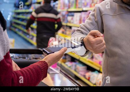 Un uomo effettua pagamenti senza contatto in una libreria o in un negozio di articoli da regalo utilizzando il suo smartwatch, utilizzando senza problemi la tecnologia NFC o WiFi, senza bisogno di ph Foto Stock