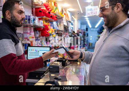 Un uomo effettua pagamenti senza contatto in una libreria o in un negozio di articoli da regalo utilizzando il proprio smartphone , utilizzando senza problemi la tecnologia NFC o WiFi, senza la necessità di p Foto Stock