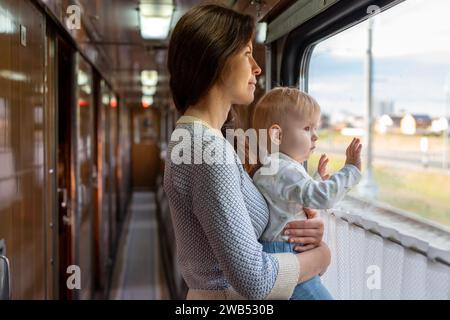 Mamma che tiene la bambina tra le braccia mentre guida su un mezzo di trasporto pubblico. Famiglia che viaggia in treno e guarda dalla finestra. Foto Stock