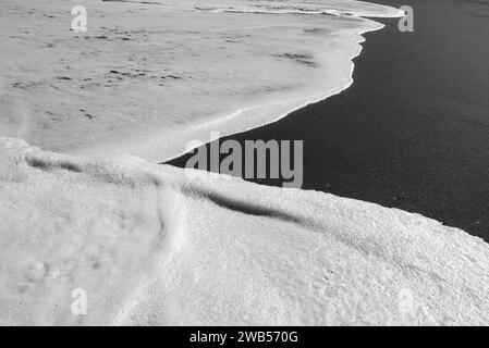 Spiaggia di sabbia nera per lo più sfocata con schiuma bianca di onde marine sullo sfondo Foto Stock