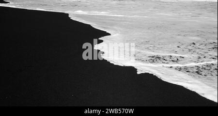 Spiaggia di sabbia nera per lo più sfocata con schiuma bianca di onde marine sullo sfondo Foto Stock