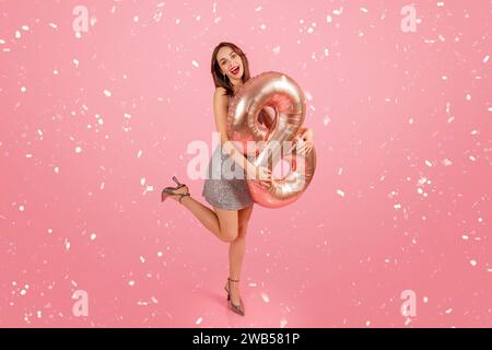 Donna gioiosa con un abito scintillante che regge un palloncino numero 9 in oro rosa Foto Stock